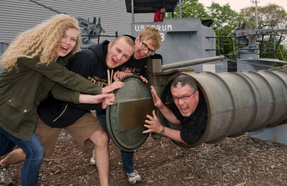 young woman with long curly blonde hair and 2 blonde young men are stuffing man into torpedo tube on USS Silversides submarine Museum