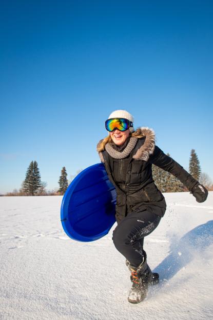 A woman gets a running start on her blue sled.