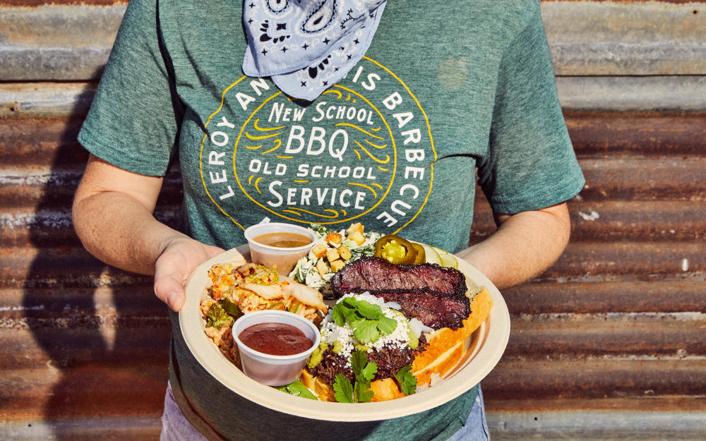 Person in Leroy and Lewis merch holding plate of barbecue and sides