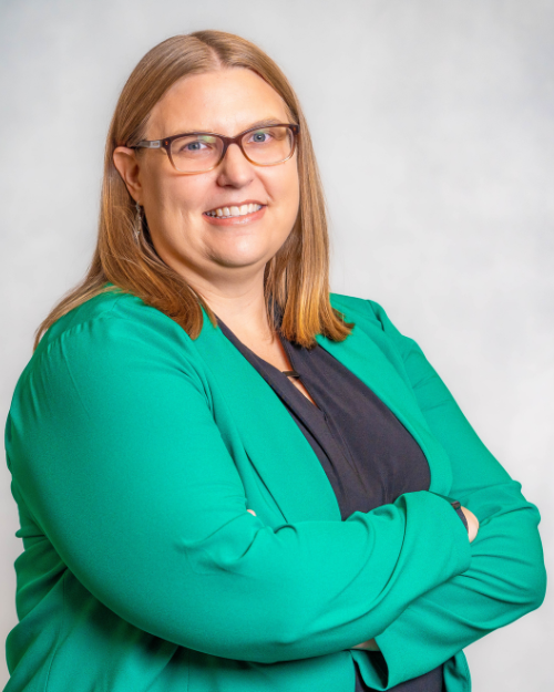 Woman wearing green blazer, smiling, brown glasses