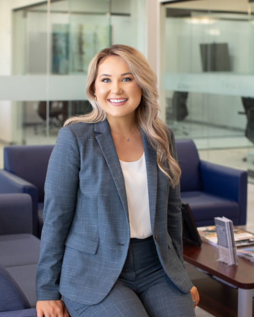 Professional headshot of a woman, with blonde hair, smiling, wearing a blue blazer/pant suit.