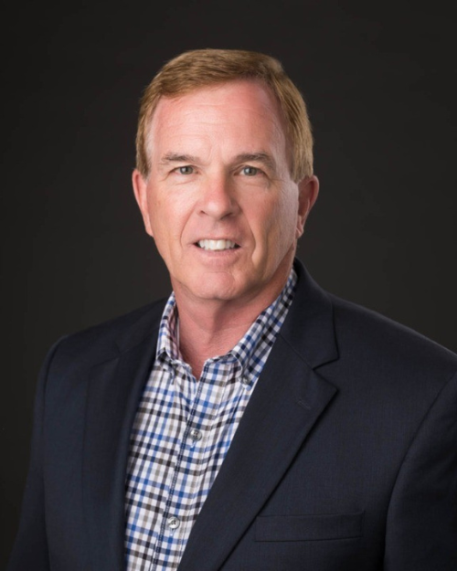 Professional headshot of man wearing black suit with checkered blue button down.