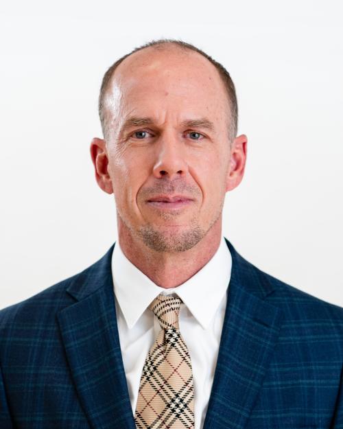 Headshot of a half-smiling man wearing a navy plaid suit with white shirt and tie