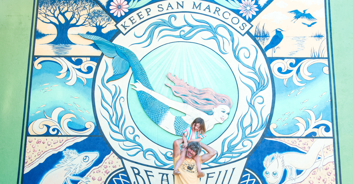 Father and daughter pose in front of a mural of a mermaid.