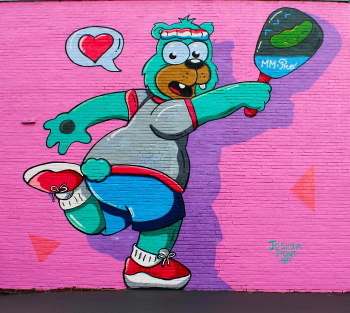 green cartoon bear playing pickleball painted onto a pink wall