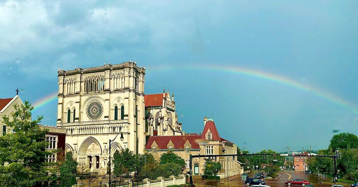 The outside of the Cathedral Basilica of the Assumption, modeled on Notre Dame Cathedral in Paris, with a rainbow in the background