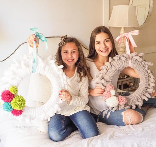 Two young girls show off their completed wreaths from the AR Workshop DIY Kits.