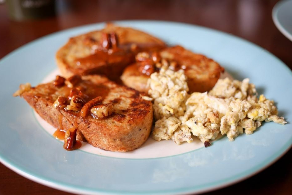 A plate of French toast topped with pecans and syrup next to a serving of scrambled eggs.