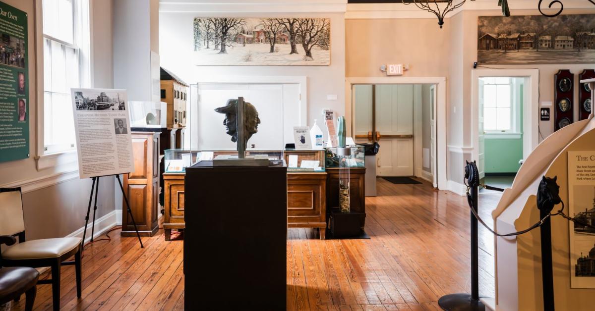 Interior image of an open room with a wooden floor, sculpture on display, artwork on the walls, and interpretive panels