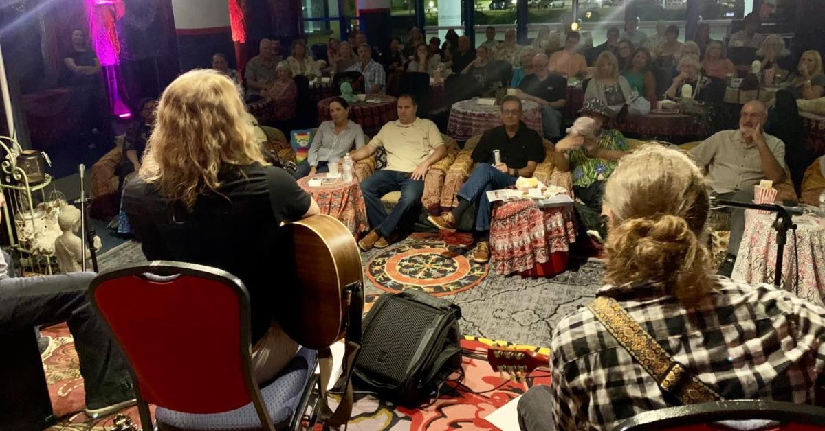 View from the stage at The Lobby Lounge in The Harbor Center, showing musicians performing to an intimate seated audience gathered around small tables in a cozy, listening-room setting.