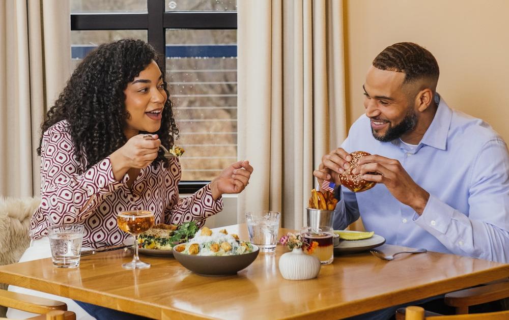 A man and woman sit at a taple and enjoy a meal while chatting.
