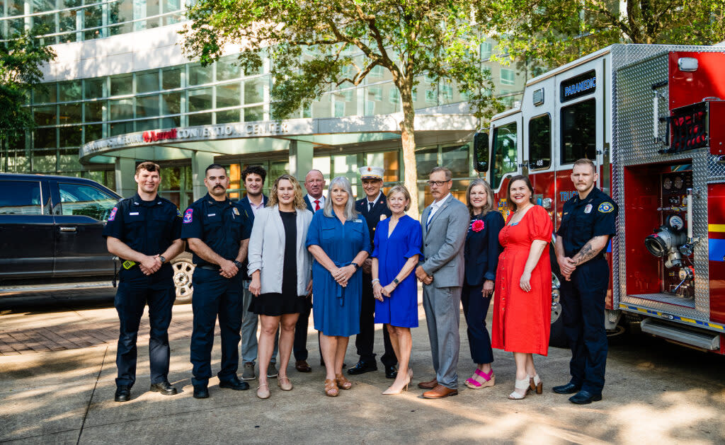 Twelve people stand in front of a fire truck at The Woodlands Waterway Marriott for the Texas State Association of Fire Fighters (TSAFF) 49th Biennial Convention. Featured are: two male firefighters, Ryan Greenwood, Josie Lewis, TWPFFA President Erik Secrest, Julie Quinn, Fire Chief Palmer Buck, Linda Nelson, (a man in a gray suit), Ashley Fenner, Elizabeth Eddins, and another firefighter.