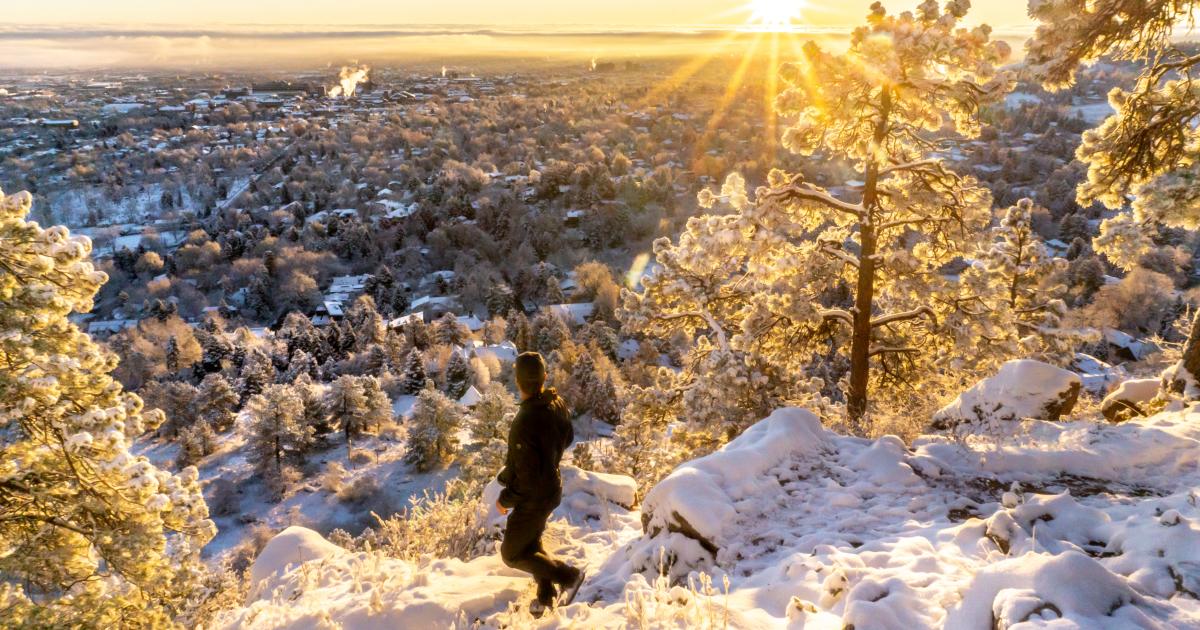 A person looking out at a spectacular view of Boulder as the sun rises while on a winter hike.