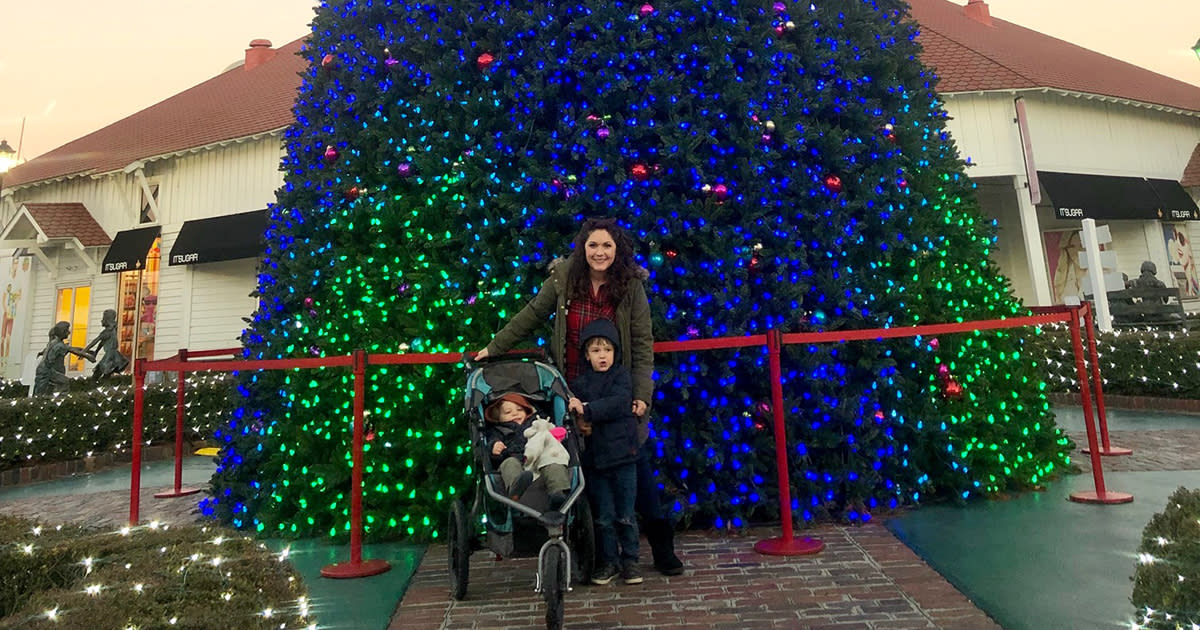 A mother with two small children - one standing and one in a stroller - in front of the Broadway at the Beach Christmas Tree
