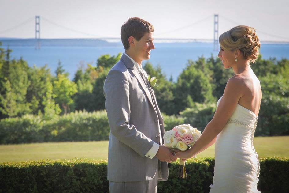 A bride and groom hold hands during their Mackinac Island wedding ceremony overlooking the water and the Mackinac Bridge