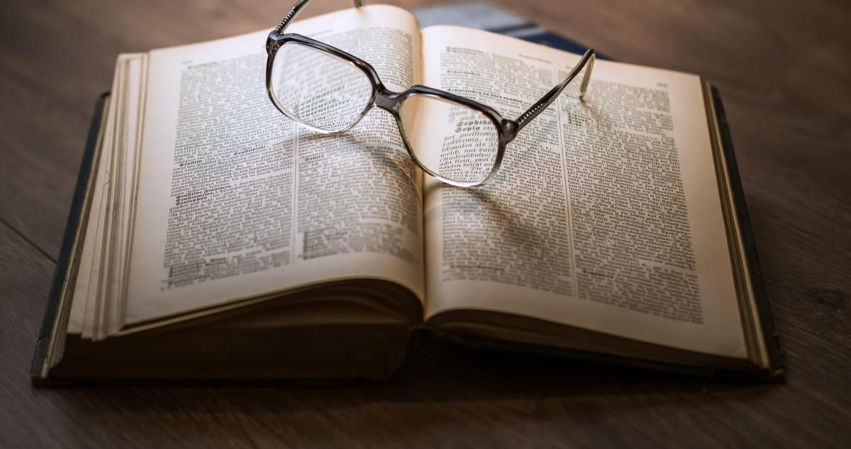 A pair of glasses resting on the middle of an open book.