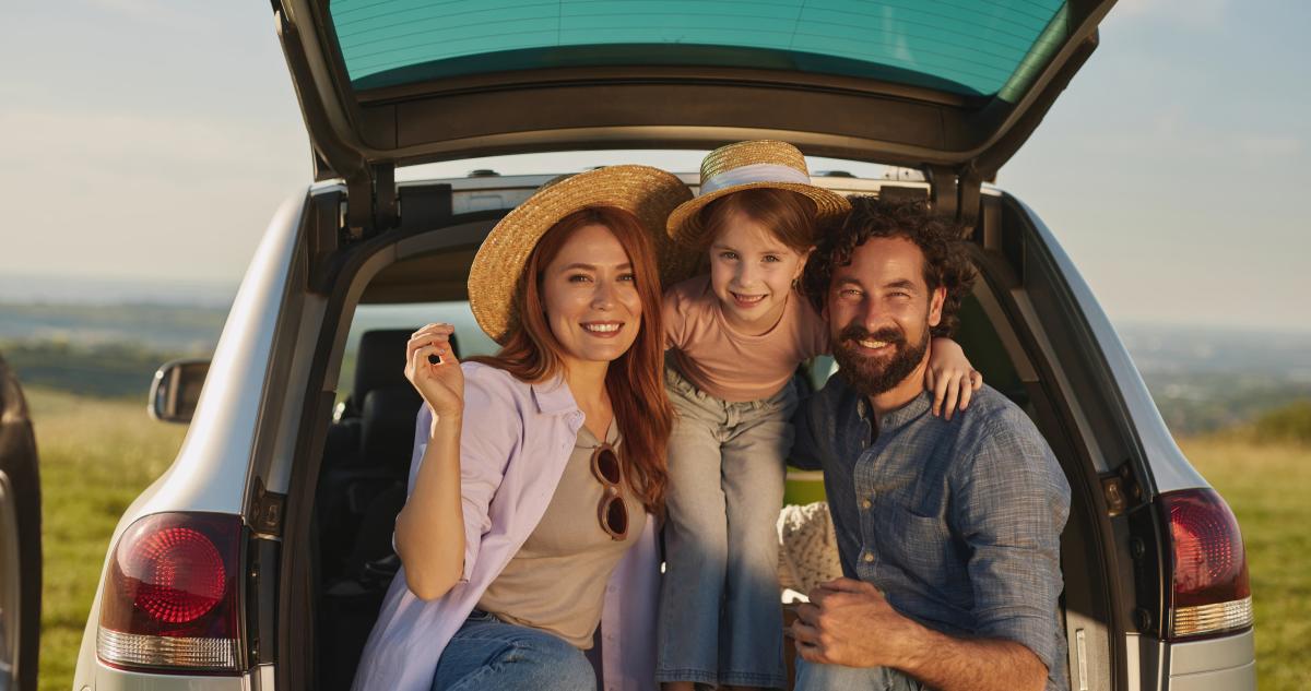 A family of three sits on the back of their hatchback vehicle.