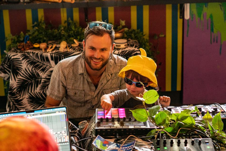A son plays with a digital music instrument while dad smiles.