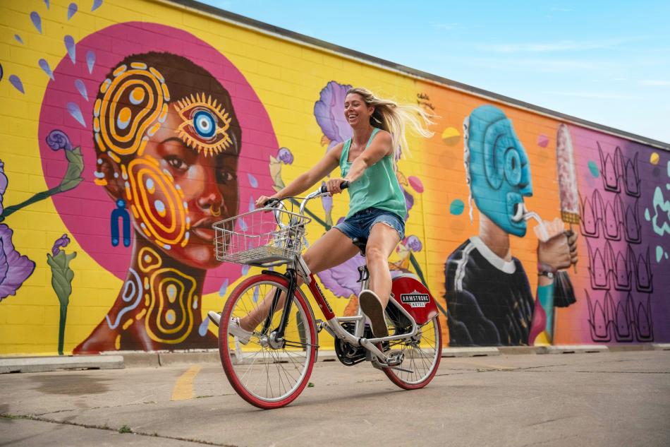 A woman rides her bike in front of an art mural downtown