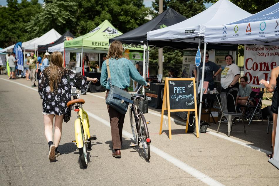 A couple walking their bikes along exhibit booths at Poudre RiverFest