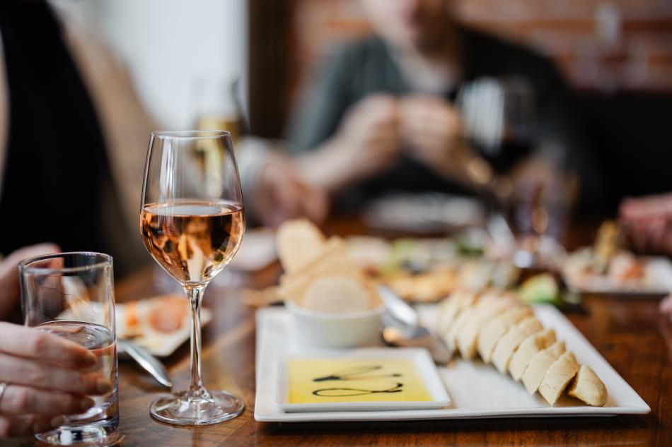 A group of people dining with wine, water glasses and a charcuterie board with a baguette and olive oil to dip