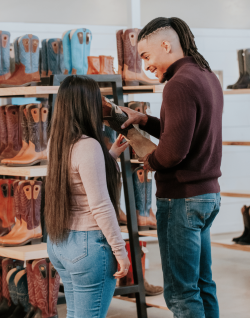 young African American man with braids smiling at his Latino wife with beautiful long dark hair as they shop for a pair of cowboy boots.