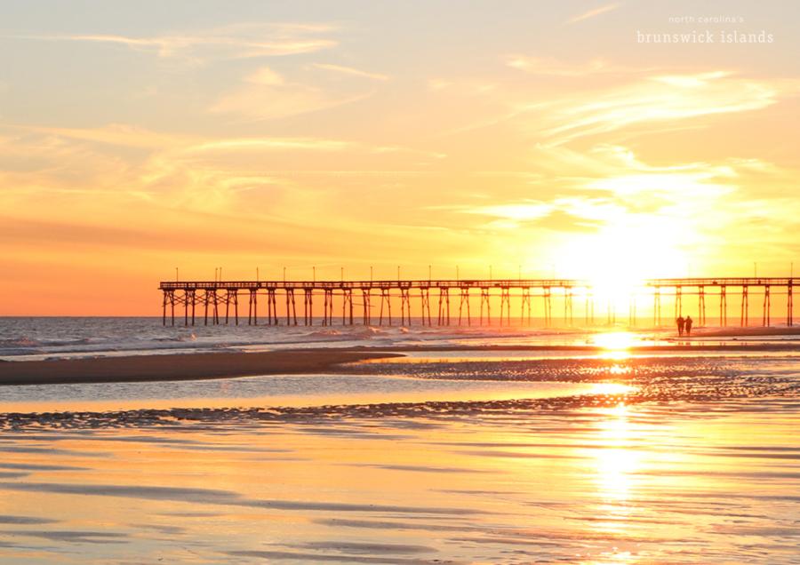 view of a pier and couple walking as the sun sets over the ocean