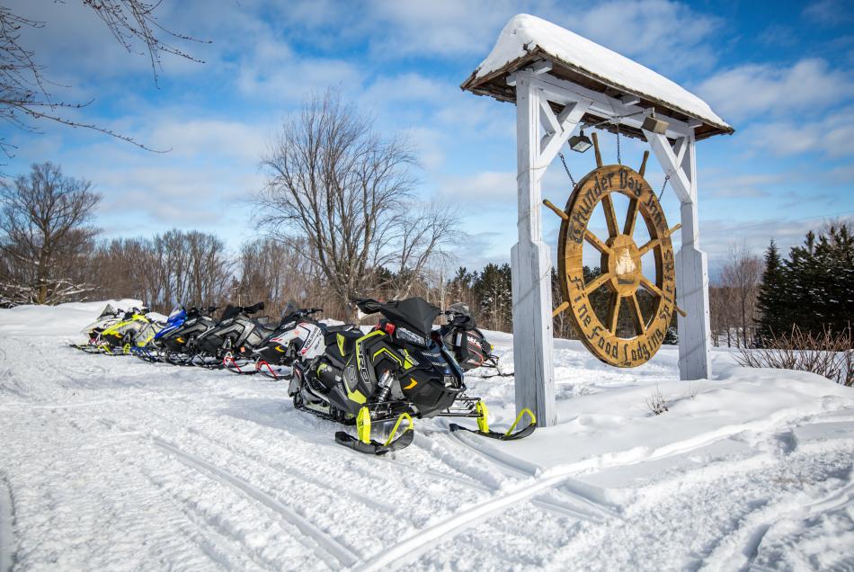 Snowmobiles lined up by Thunder Bay Inn's entrance sign.