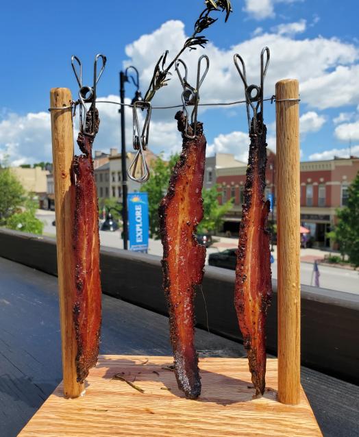 Three strips of bacon hanging on a line with clothes pins with a view of Main Street Canandaigua in the background
