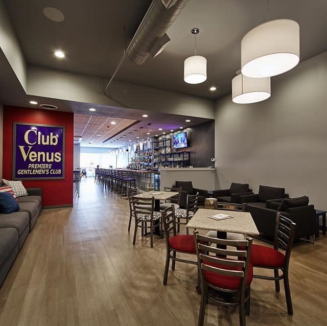 Inside The Globe Covington bar, with long modern bar, wood floors, red-seat chairs, and the old blue Club Venus sign on the wall