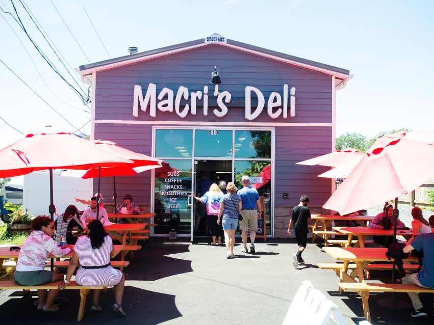 Macri's Deli exterior with people out front at picnic tables covered by umbrellas