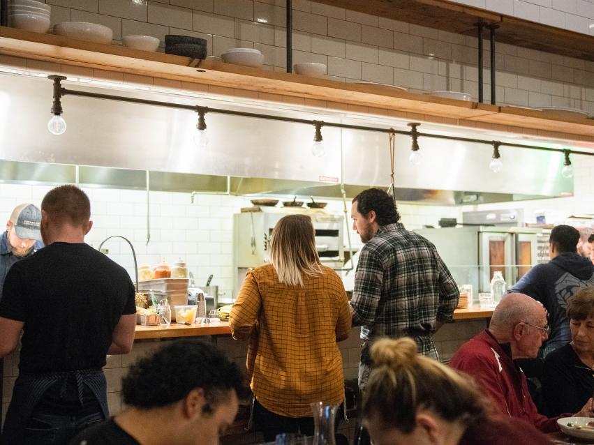 A couple sitting at a counter that overlooks the Kindred Fare kitchen operations