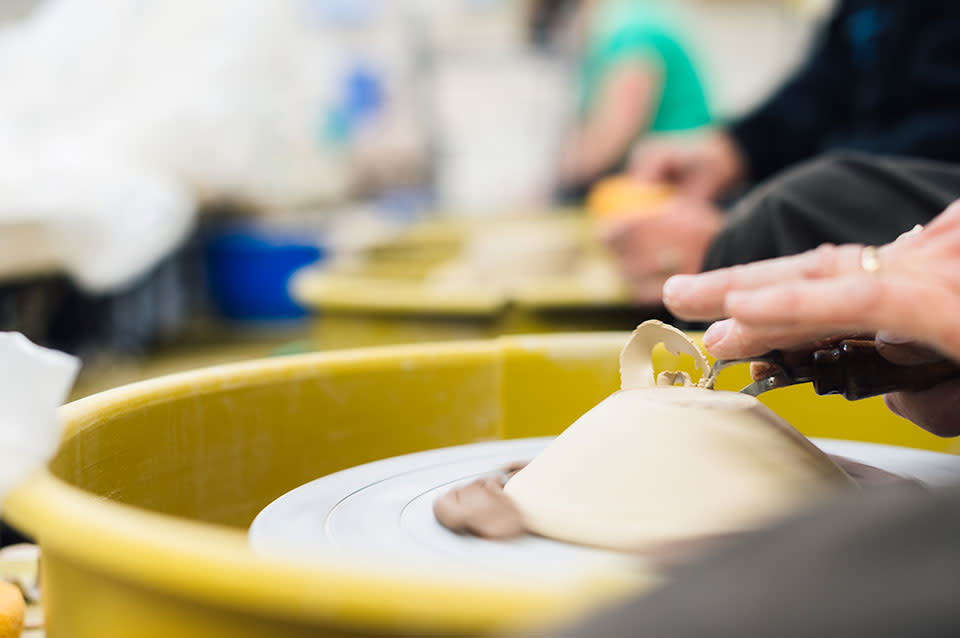 Hands throwing white clay on a yellow pottery wheel