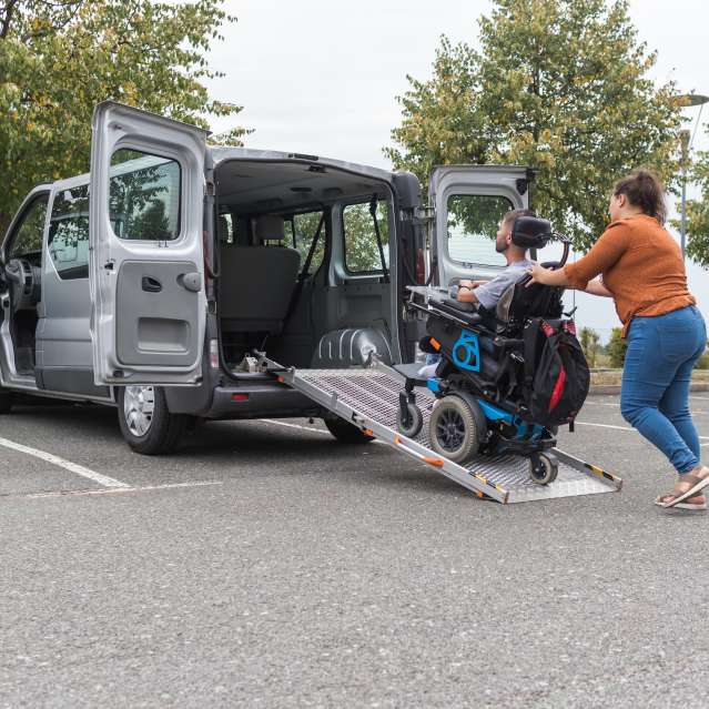 A woman helping a disabled man up a ramp and into a wheelchair accessible van.