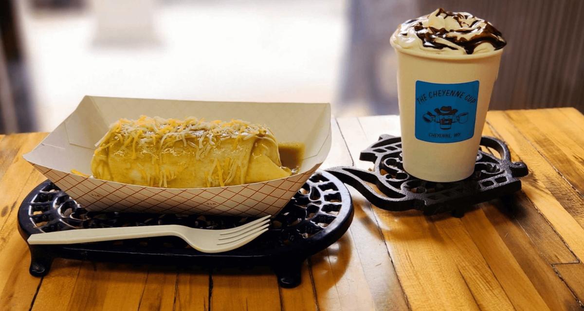 Smothered burrito and whipped cream topped mocha in 'The Cheyenne Cup' branded cup, on a wooden table at a local Cheyenne coffee shop.