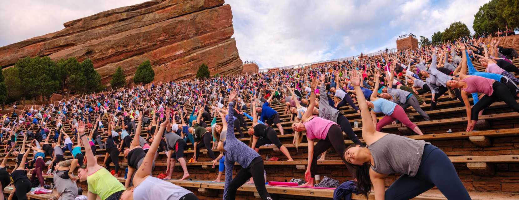 People hold a yoga pose on the seats at Red Rocks with towering fountain formation rocks in the background