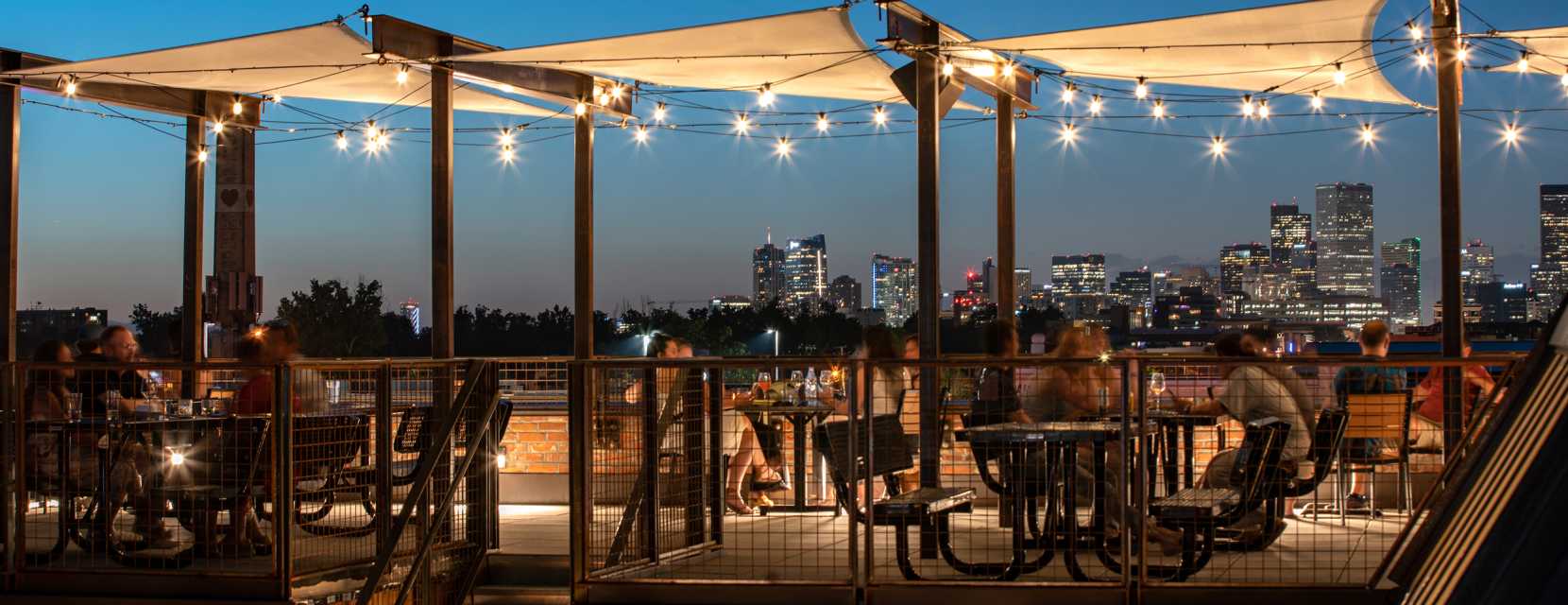 People sitting on the rooftop of BurnDown and enjoying the Denver skyline in twilight.