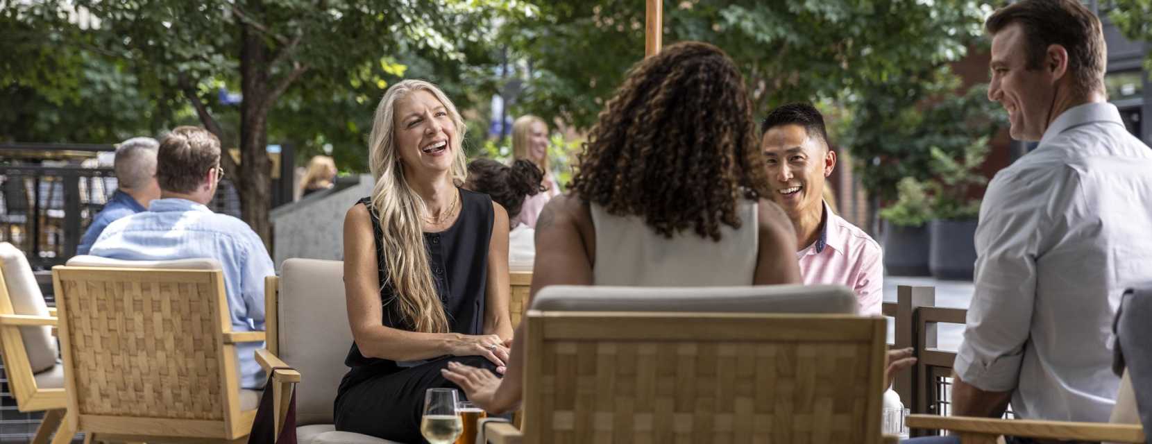 A group of people smile with beverages in front of them on the patio of Chez Maggy in downtown Denver