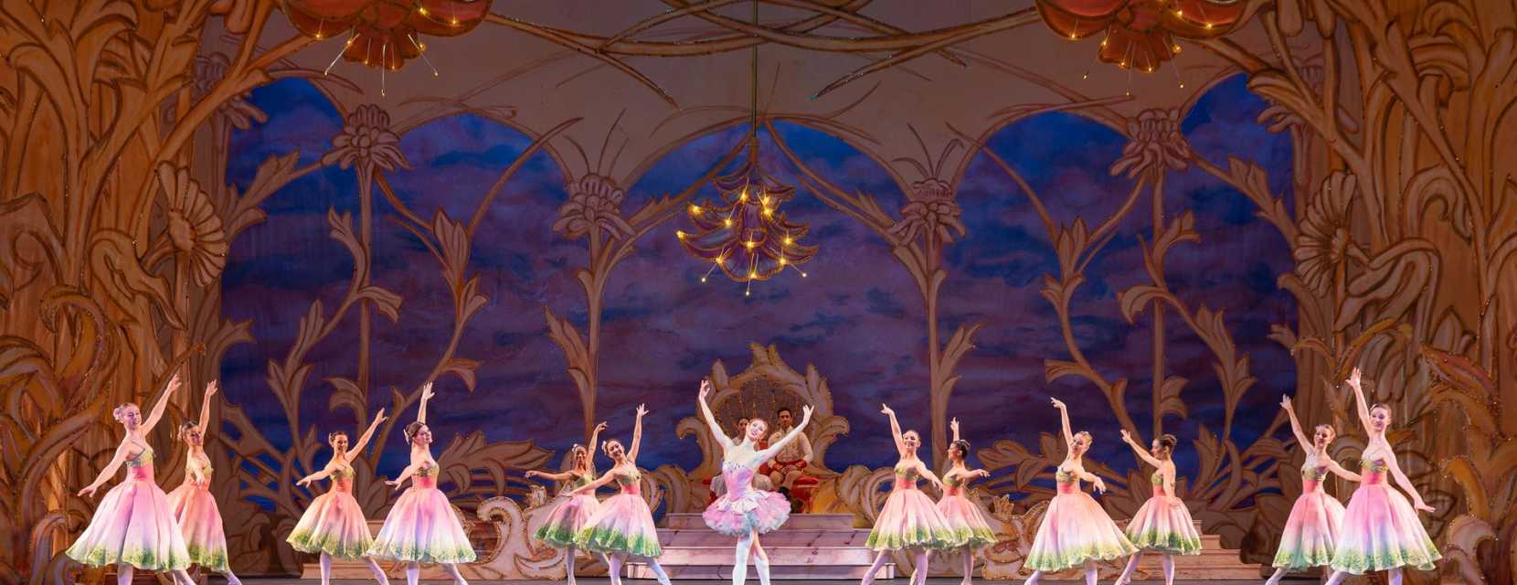 Ballet dancers wearing pink and green dresses dance across the stage