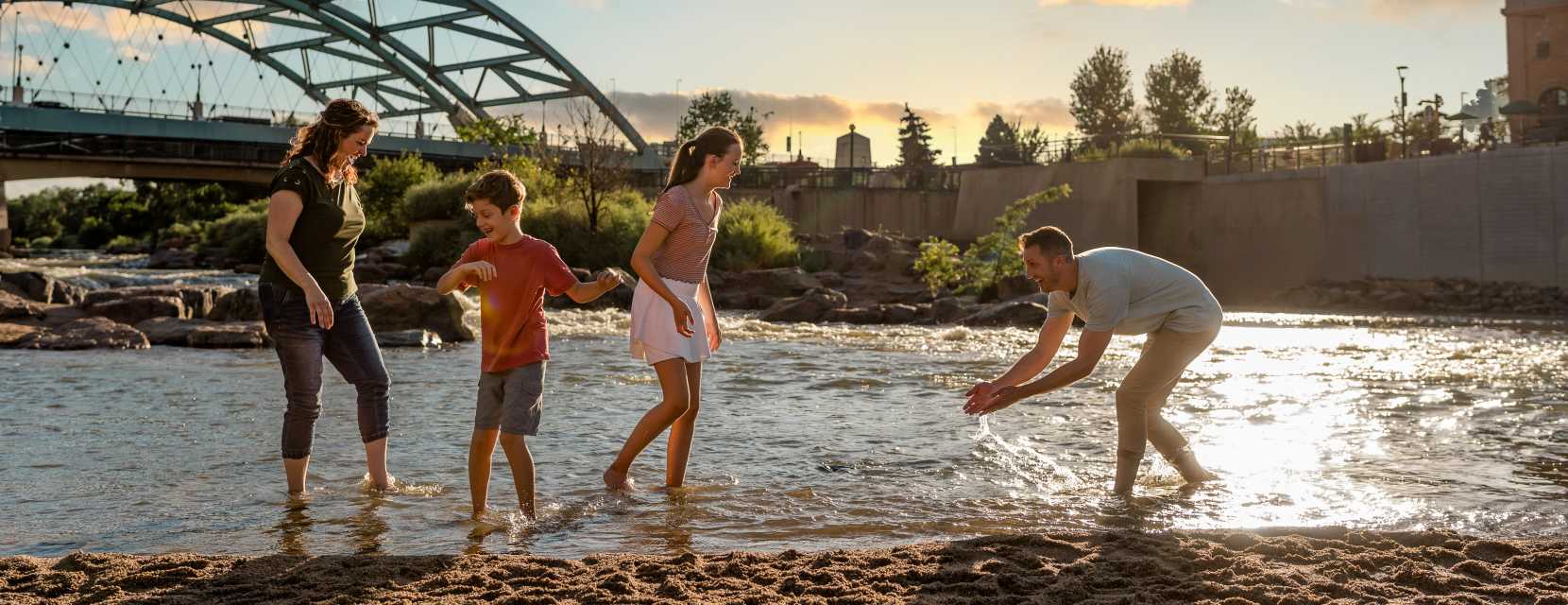 A family plays in the water near a sandy beach at Confluence Park in Denver, Colorado.