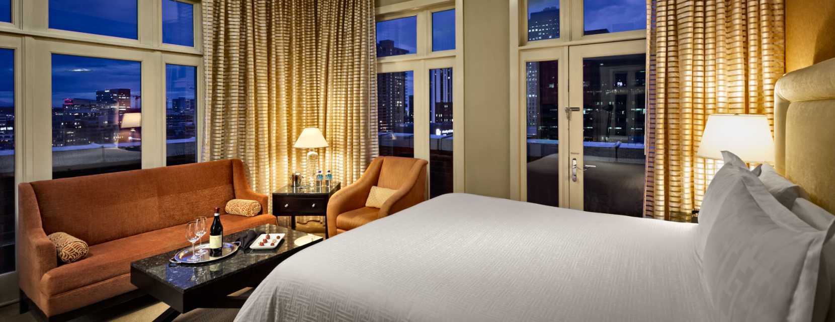 A guest room at Hotel Teatro in Denver, Colorado, with a bottle of wine and chocolate on the coffee table.