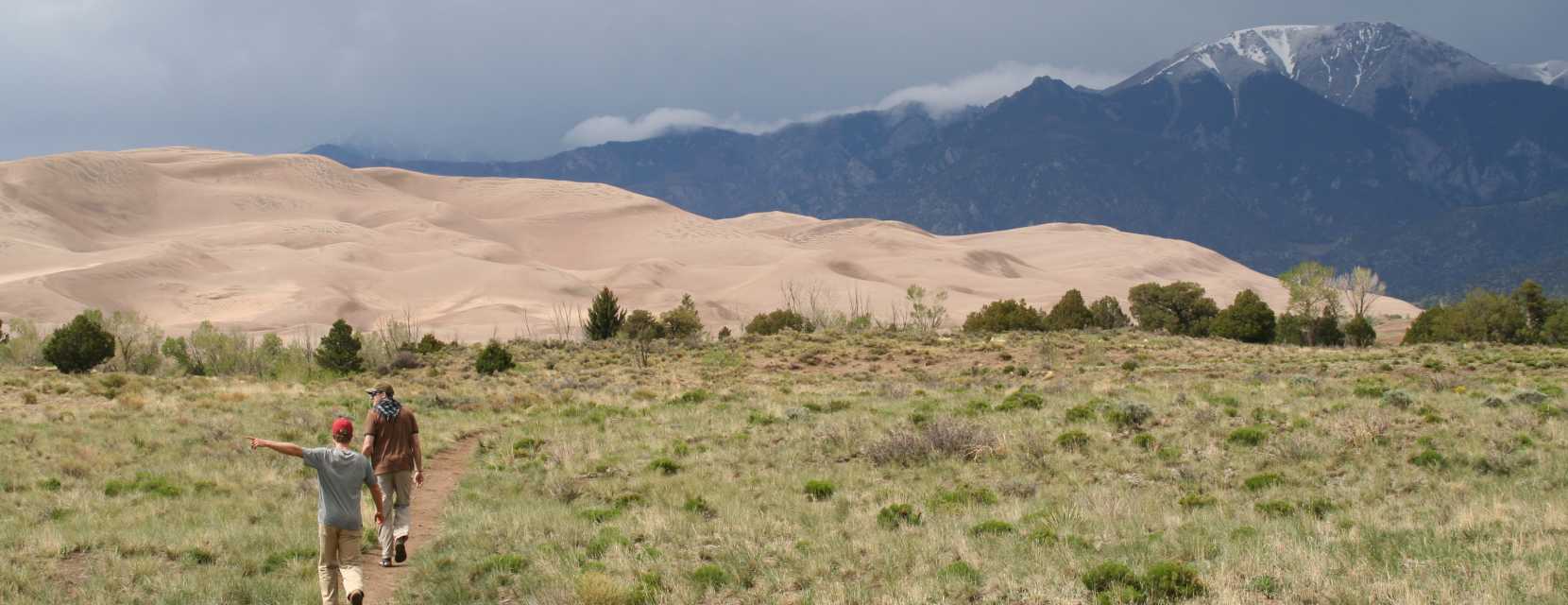 Two people walking on a trail toward the dunes at Great Sand Dunes National Park and Preserve.