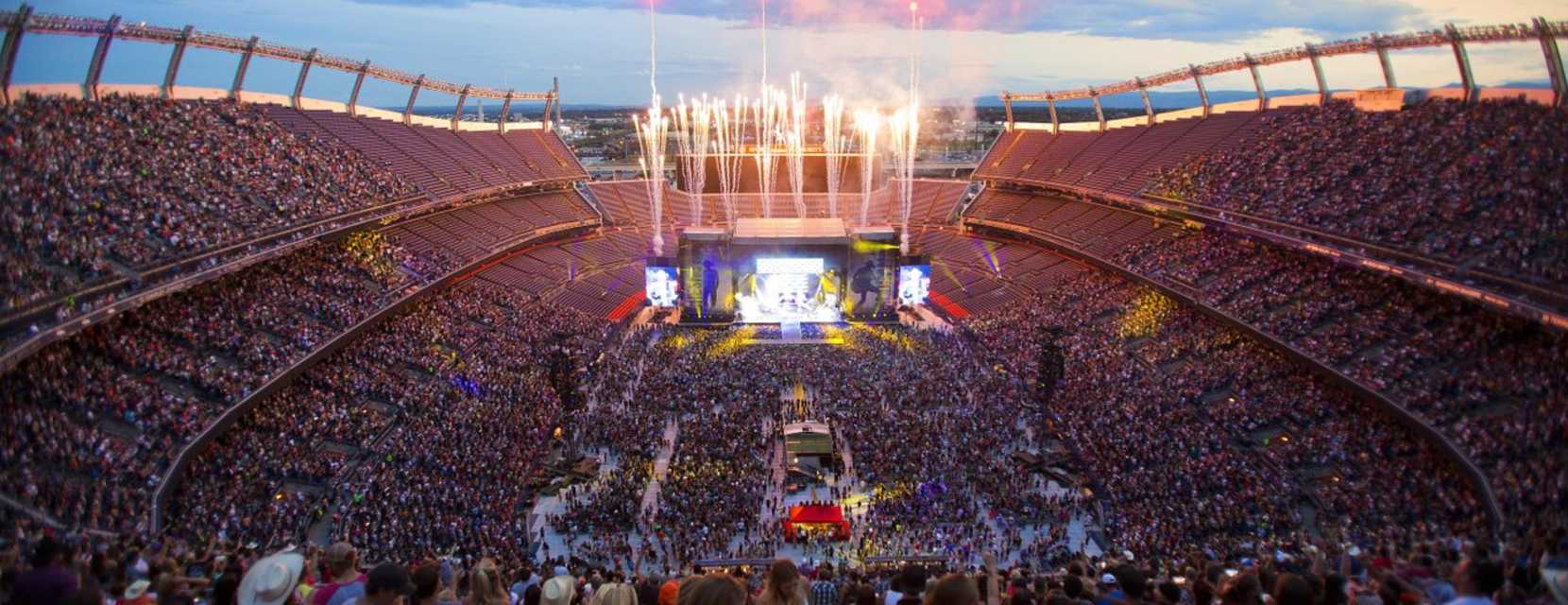 Fireworks explode over Empower Field at sunset during a concert