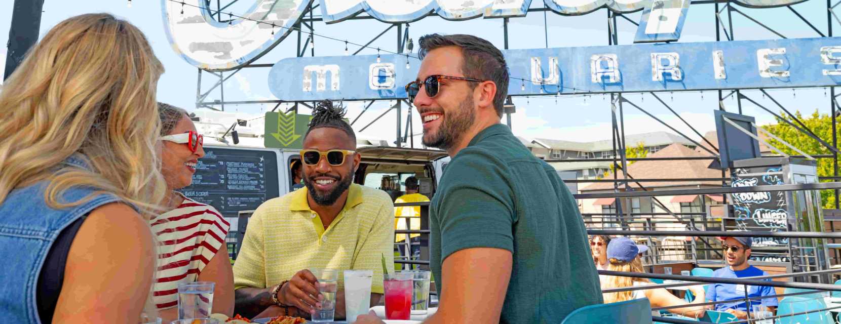 A group smiles while sipping drinks with appetizers on the table at Linger in Denver