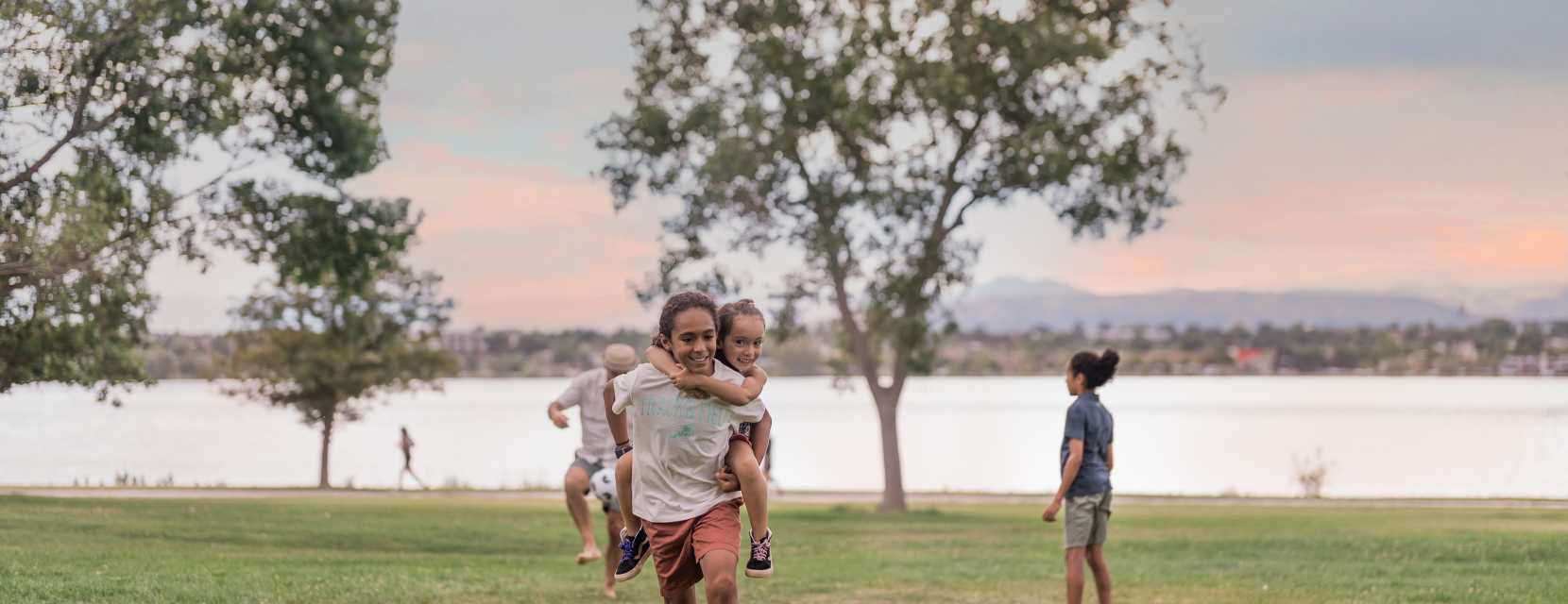 A family plays in the grass at Sloan’s Lake Park with the lake and mountains in the background.