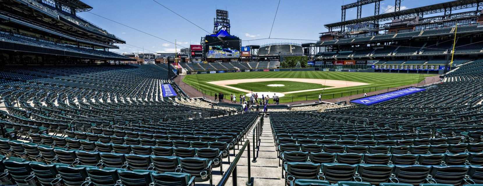 Empty seats lined up in front of the baseball diamond at Coors Field on a blue-sky day.