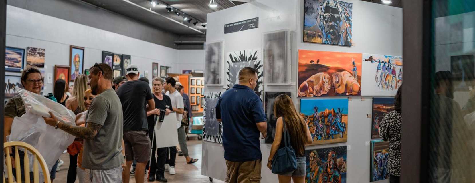 People gaze at paintings displayed in a gallery at at First Friday art walk