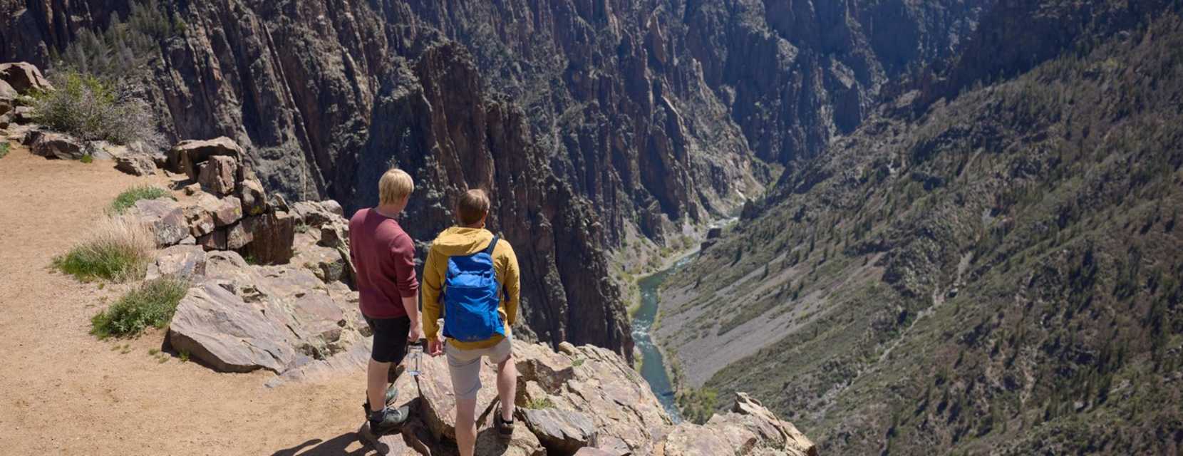 Two people gaze over the edge of Black Canyon on the Gunnison, where a river cuts through the rock