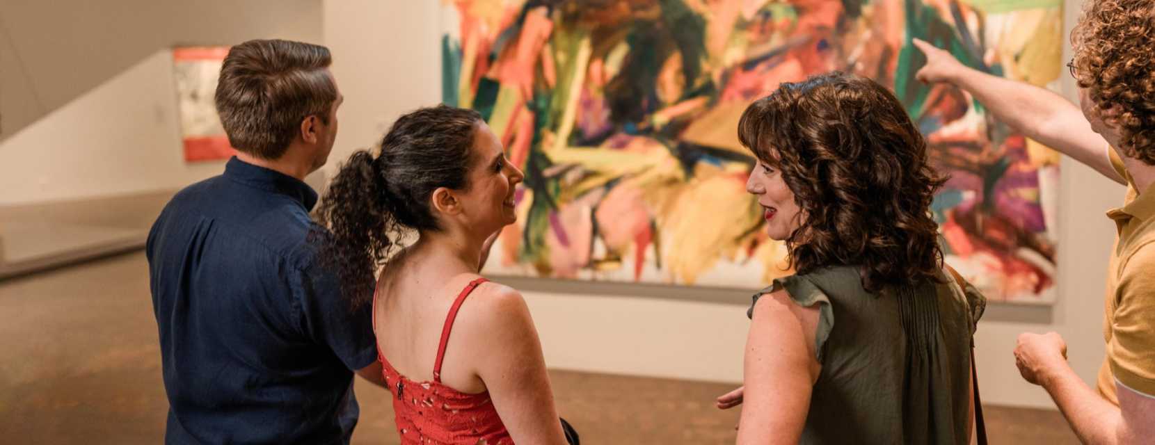 A group of people smile and talk about a colorful abstract painting at the Denver Art Museum