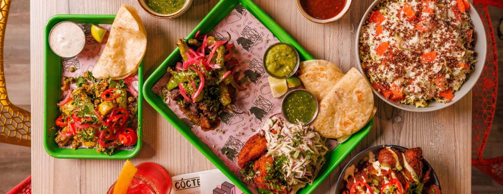 A table is filled with fresh tacos, nachos, salsa and cocktails